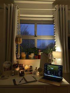 a laptop computer sitting on top of a desk next to a window covered in blinds