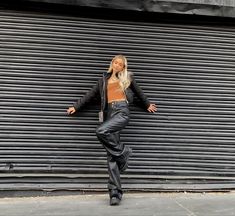 a woman leaning against a wall wearing black leather pants and a cropped brown top