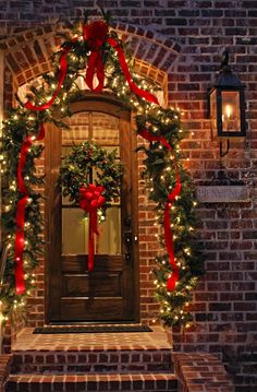 a christmas wreath on the front door of a brick house with lights and garlands around it