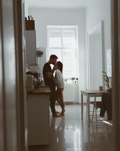 two people standing in a kitchen next to each other with one kissing the other's head