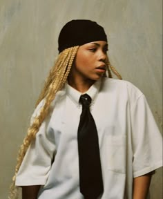 a young woman with long blonde hair wearing a black tie and white shirt, standing in front of a wall