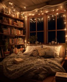 an unmade bed in front of a window with lights strung from the ceiling and bookshelves