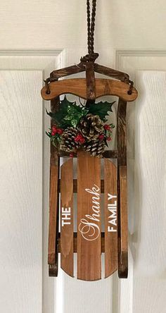 a wooden sled hanging from the side of a door decorated with holly and pine cones