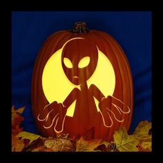 a pumpkin with an alien carved into it's face and hands in front of leaves