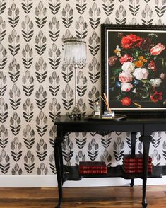 a black table with flowers on it in front of a wallpapered background and lamp