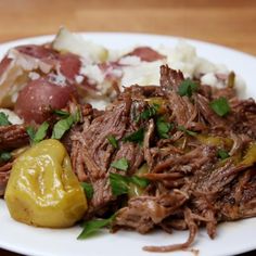 a white plate topped with meat, potatoes and green peppers on top of a wooden table