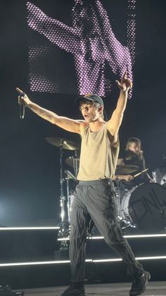 a male in a tan shirt and black pants is on stage with his arms up