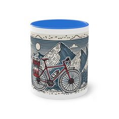 a blue and white coffee mug with a bicycle on the front, mountains in the background