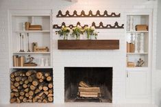 a fireplace with white brick and wooden shelves filled with books, logs and flowers on the mantel