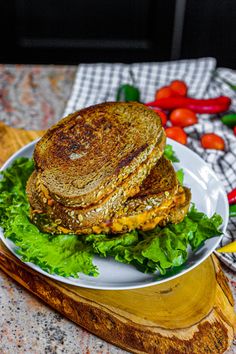 a sandwich is on a white plate with lettuce and tomatoes in the background