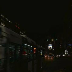 a city street at night with cars and buses passing by in the dark, blurry image