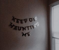 a sign that says keep on hanging me in the corner of a room next to a window