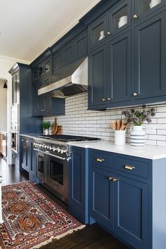 a kitchen with dark blue cabinets and white subway backsplash, gold pulls on the hood