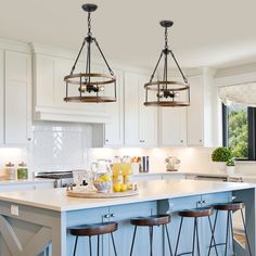 two chandeliers hanging from the ceiling over a kitchen island with bar stools