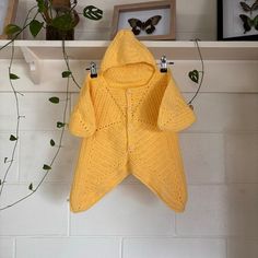 a crocheted yellow sweater hanging on a white brick wall next to potted plants