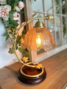 a table lamp sitting on top of a wooden table next to a vase with flowers