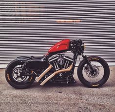 a red and black motorcycle parked in front of a garage door with roller shutters