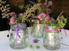 three mason jars filled with flowers and candles on a white table cloth covered tablecloth