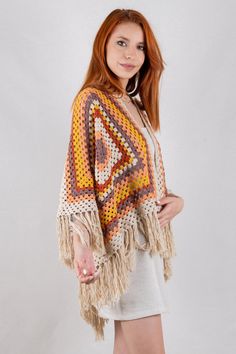 a woman is posing for the camera wearing a crocheted shawl with fringes