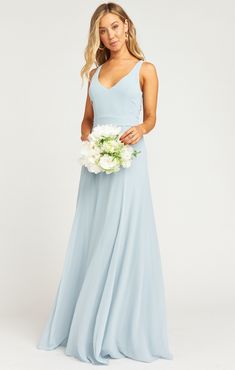 a woman in a long blue dress holding a white bouquet and posing for the camera