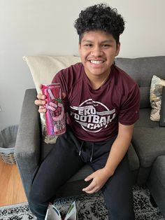 a young man sitting on a couch holding up a can of soda and a drink