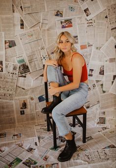 a woman is sitting on a chair in front of a wall covered with newspaper pages