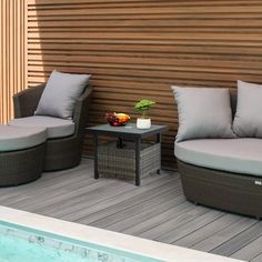 two couches and a table on a deck next to a swimming pool with wood slats