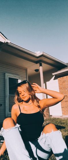 a woman sitting on the grass in front of a house with her hands behind her head