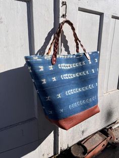 The Thalia Tote is an oversized fun time. This giant tote will give you extra joy every time you head out for an adventure. Made with vintage indigo dyed cotton fabric that is hand printed from Ghana, lined in ticking stripe, buffalo leather at the bottom, sturdy Latigo braided handles, and copper rivets. The lining has three pockets sized for an i-phone, a water bottle, and a magazine. The bag itself can hold blankets, towels, pic-nic supplies or anything you need to tote around for a fun day out. Hidden interior details: The indigo fabric is fused to an extra thick padded interlining then faced with a cotton canvas giving the tote structure. There is a Latigo (thick saddle leather) footing sandwiched between the buffalo leather and lining.  The fabric is vintage and hand printed which me Indigo Cotton Bag For Everyday Use, Everyday Indigo Cotton Bag, Blue Cotton Bags With Leather Handles, Bohemian Blue Canvas Bag For Everyday Use, Casual Indigo Bags For Everyday Use, Bohemian Blue Canvas Bag, Casual Indigo Cotton Bag, Indigo Casual Bag For Daily Use, Casual Indigo Bags For Daily Use