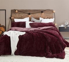 a bedroom with a bed covered in a maroon comforter and white pillows on top of it