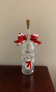 a glass bottle with a red ribbon and snowman on it that says let it snow