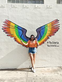 a woman standing in front of a wall with a painted bird on it's wings