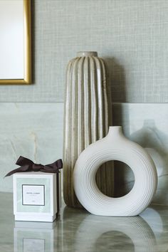 a white vase sitting on top of a table next to a box with a brown bow