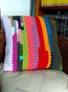 a multicolored crocheted pillow sitting on top of a couch next to a book shelf