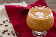 a glass filled with liquid sitting on top of a red cloth next to coffee beans