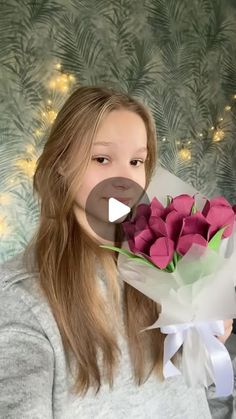 a woman holding a bouquet of pink roses in front of a wall with christmas lights