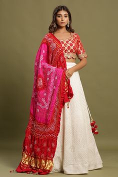 Shop White self-embroidered Zari lehenga set featuring bandhej dual print dupatta and zari & gota patti embroidered red blouse. The lehenga also has a long tassel attached to tie the knot. Pair it with beautiful jewelry to enhance your look. Shop online from Pure Elegance. White Bandhani Print Lehenga For Wedding, Red Bandhani Lehenga, Red And White Lehenga, White Silk Lehenga, White Bandhani Print Dupatta, White Bandhani Print Lehenga, Red Semi-stitched Bohemian Lehenga, Zari Lehenga, Bandhej Print