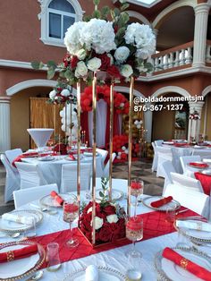 a table set up for a wedding with red and white flowers on the centerpiece