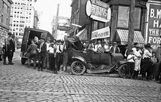 an old black and white photo of people standing in front of a car on the street