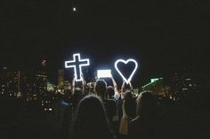 people standing in the dark holding up crosses and heart shaped lights with buildings in the background