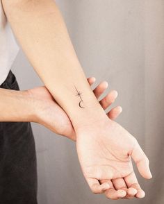 two hands holding each other with a small cross tattoo on the wrist and an arrow in the middle