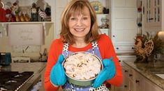 a woman in an apron holding a bowl with food on it while standing in a kitchen