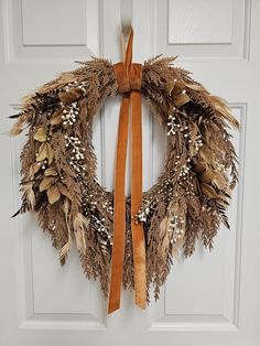 a wreath is hanging on the front door with a brown ribbon and some dried leaves