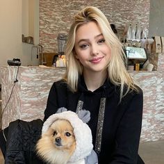 a woman sitting on a chair holding a small dog in her lap and wearing a sweater