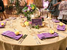 the table is set with purple napkins and place settings for guests to sit at