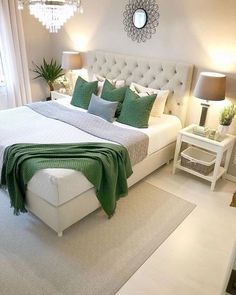 a bedroom with a white bed and green pillows on the headboard, along with a chandelier