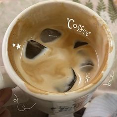 a person holding a cup of coffee with their face drawn on the foam in front of them