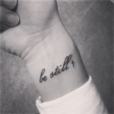 a black and white photo of a person's wrist with the word be still on it