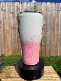 a pink and white cup sitting on top of a wooden table next to a fence