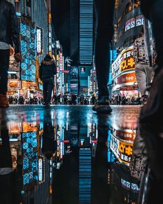 people are walking on the street at night in times square, with brightly lit buildings